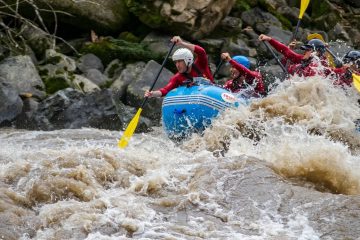 Grupo haciendo rafting en aguas bravas del río Namangoza, equipo de seguridad y cascos, paisaje tropical de fondo