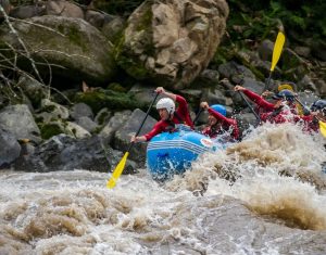 Grupo haciendo rafting en aguas bravas del río Namangoza, equipo de seguridad y cascos, paisaje tropical de fondo