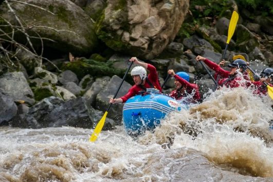 Grupo haciendo rafting en aguas bravas del río Namangoza, equipo de seguridad y cascos, paisaje tropical de fondo