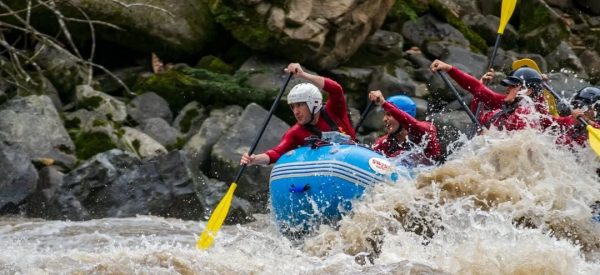 Grupo haciendo rafting en aguas bravas del río Namangoza, equipo de seguridad y cascos, paisaje tropical de fondo